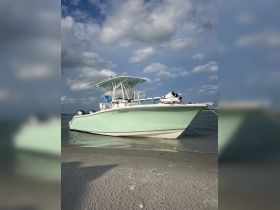 A sleek speedboat rests on the sandy shore, showcasing its elegant design against a backdrop of blue skies and fluffy clouds — perfect for a day of adventure on the water.