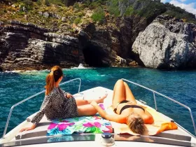 Two friends relax and sunbathe on the deck of a boat, surrounded by stunning coastal scenery — a perfect getaway for sun and sea lovers.
