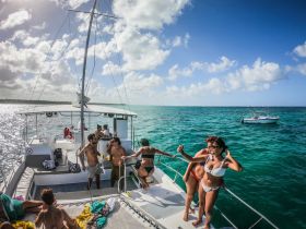 A lively group enjoys a fun day on a catamaran, capturing memories with selfies against a stunning turquoise backdrop — perfect for celebrations and group outings.