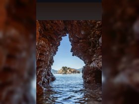 A stunning view of an island framed by rocky formations, showcasing the beautiful coastline and crystal-clear waters — a perfect destination for boat tours and scenic explorations.
