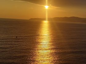 A stunning sunset casts golden reflections over the ocean, with a distant island silhouette enhancing the serene atmosphere — perfect for romantic evenings or peaceful retreats.