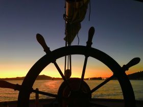A captivating view of a ship's helm silhouetted against a stunning sunset, showcasing the beauty of navigating the waters during twilight.