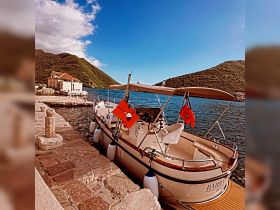 A charming boat docked by the waterfront, surrounded by scenic hills and clear blue skies, perfect for exploring coastal destinations.