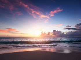A stunning sunset over the ocean, casting vibrant colors across the sky and reflecting on the beach — a perfect backdrop for serene moments and picturesque views.