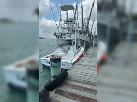 A fishing boat named 'E.A. II' docked at the pier, showcasing its structure against a backdrop of other vessels and a cloudy sky.