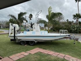 A center console boat with a Suzuki engine parked on a trailer, surrounded by palm trees, showcasing its sleek design and readiness for adventure.