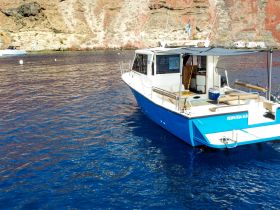 A clear view of a boat named 'ΠΕΙΡΑΤΕΙΑ Ν.Θ.' navigating through calm blue waters, set against a stunning rocky backdrop — ideal for exploring coastal destinations.