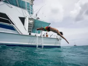 A young boy dives off the side of a boat into the clear turquoise waters, capturing the excitement of summer water activities and fun on the water.