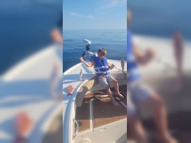 A young boy proudly displays his catch while fishing on a boat, showcasing the joy of a family fishing trip on calm waters.