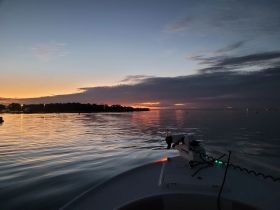 A serene sunset view from the bow of a boat, reflecting on calm waters — perfect for evening cruises and relaxation on the water.