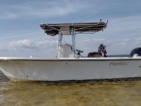 A side view of a Parker boat docked in shallow waters, showcasing its sleek design against a backdrop of blue skies and gentle waves.