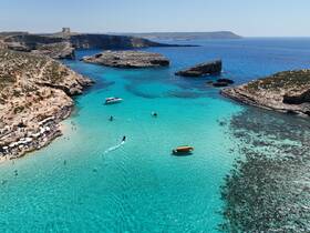 A stunning aerial view of a vibrant beach with turquoise waters, showcasing boats and people enjoying the sun — a perfect destination for water activities and relaxation.
