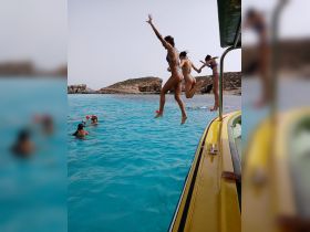 A group of friends joyfully jumps into the crystal-clear waters, capturing the essence of summer fun and adventure on a boat trip.
