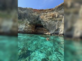 A couple enjoys a refreshing swim in crystal-clear waters near a stunning cave, showcasing the beauty of nature and adventure on the water.
