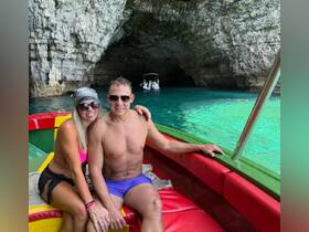 A couple enjoys a scenic moment aboard a colorful boat inside a stunning cave, surrounded by crystal-clear waters — perfect for adventure seekers and romantic getaways.