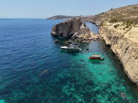 A stunning view of boats anchored near a rocky coastline, with a swimmer enjoying the crystal-clear waters — a perfect representation of a summer day on the water.