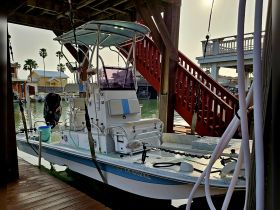 A well-maintained center console boat docked under a wooden structure, showcasing its sleek design and readiness for fishing or leisure outings.