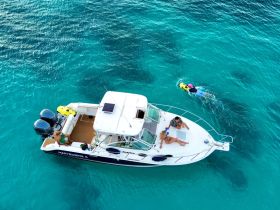 A lively scene featuring a group enjoying their time on a boat, with one person swimming nearby in the clear turquoise waters — perfect for a fun day out on the water.