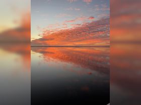 A breathtaking sunset casts vibrant colors across the sky and reflects beautifully on the calm water, creating a serene and picturesque scene perfect for nature lovers.