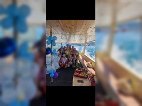 A lively group celebrates aboard a boat, adorned with decorations and enjoying a variety of fresh fruits — perfect for festive gatherings on the water.