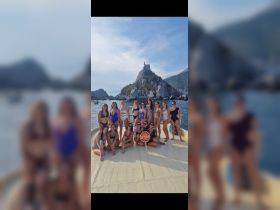 A lively group of women poses on the deck of a boat, celebrating with a fun sign at a picturesque stop — perfect for bachelorette parties or group outings on the water.