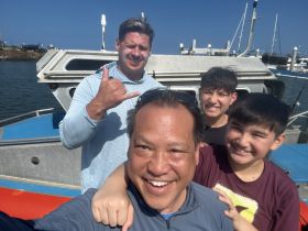 A joyful group of three, including two children, poses for a selfie on a boat, capturing a fun moment on the water.