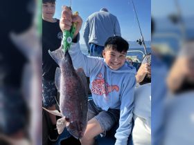 A young boy proudly displays his catch while fishing with friends on a boat, capturing the joy of a successful day on the water.