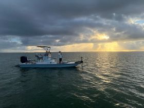 A fisherman casts his line from a boat during a stunning sunset, capturing the essence of a peaceful fishing trip on the open water.