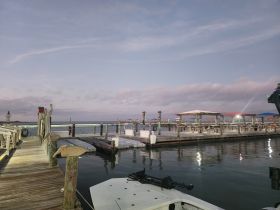 A serene view of a marina at dusk, showcasing the docks and calm waters, ideal for boat enthusiasts and evening strolls.