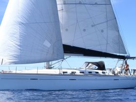 A sleek sailboat navigates the open waters with a crew member at the helm, showcasing the thrill of sailing adventures.