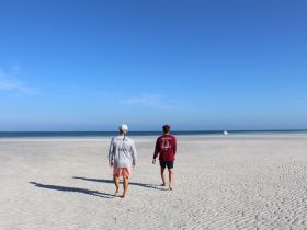 A couple strolls along a picturesque beach, with a serene ocean backdrop — perfect for capturing memorable moments during a coastal getaway.