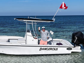 A man joyfully poses on his boat named 'DANGEROUS' while enjoying a sunny day on the water, perfect for snorkeling adventures and fun outings.