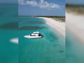 A stunning aerial view of a luxurious yacht anchored in crystal-clear turquoise waters, surrounded by a pristine white sandy beach — perfect for a serene getaway.