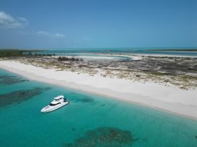 A stunning aerial view of a luxurious yacht anchored in crystal-clear turquoise waters, surrounded by pristine white sandy beaches — an ideal setting for a relaxing getaway.