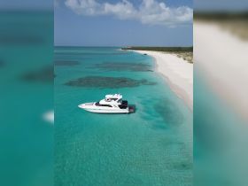 A stunning aerial view of a luxurious yacht anchored in crystal-clear turquoise waters, showcasing the beauty of a serene beach backdrop.