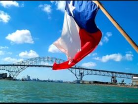 A vibrant view of the Texas flag waving in the breeze with a scenic bridge in the background, capturing the essence of a beautiful day on the water.