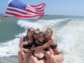 A fun group of friends enjoys a sunny day on the water, celebrating with laughter and the American flag waving in the breeze — perfect for summer boating adventures.