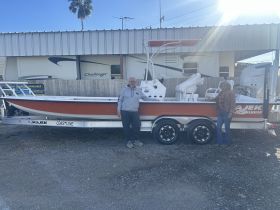 Two individuals stand beside a Majek Coastline boat, showcasing its sleek design while docked — perfect for fishing or leisure outings.