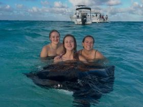 Three friends enjoy a memorable encounter swimming with a stingray in crystal-clear waters, showcasing the thrill of wildlife interactions in tropical destinations.