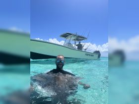 A man interacts closely with a stingray while swimming in crystal-clear waters, showcasing a unique wildlife experience in a tropical paradise.