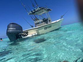 A fishing boat named 'Fish'n Hips' is anchored in crystal-clear waters, showcasing its sleek design and fishing gear, perfect for a day of adventure on the water.