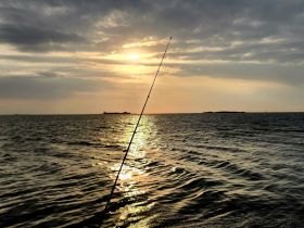 A serene sunset view over the water with a fishing rod silhouetted against the glowing horizon, perfect for capturing the essence of a peaceful fishing trip.