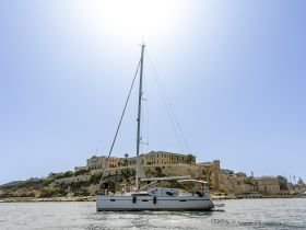 A lively group enjoys a sailing experience aboard a yacht, with a stunning historic landmark in the background — perfect for exploring coastal destinations.