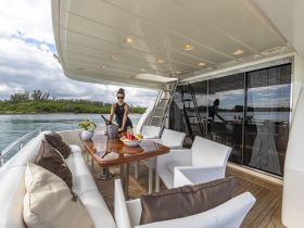 A stylish interior view of a yacht's dining area, featuring a woman preparing refreshments with a scenic backdrop of the water and greenery — perfect for luxurious onboard experiences.