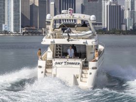 A stylish yacht named 'Salt Shaker' cruises through the waters of Miami, showcasing a lively group enjoying their time on the water against a stunning city backdrop.