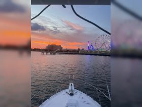 A stunning sunset view from the bow of a boat, overlooking a vibrant harbor with a ferris wheel and colorful lights — perfect for evening cruises.