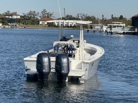 A sleek center console boat is docked in calm waters, showcasing its powerful twin engines and modern design — perfect for fishing or leisure outings.