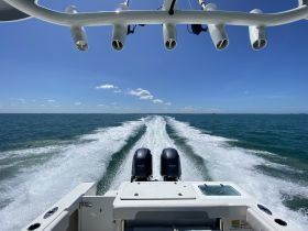 A dynamic view from the back of a speedboat cruising through clear waters, showcasing the boat's powerful engines and the wake it creates.