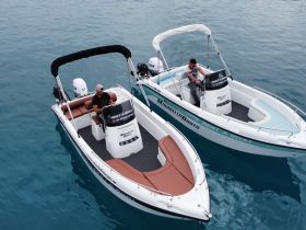 Two men operate rental boats in clear turquoise waters, showcasing a perfect day for boating adventures. Ideal for exploring coastal destinations or enjoying water sports.