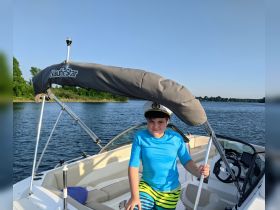 A young boy wearing a captain's hat stands at the helm of a NauticStar boat, ready for a fun day on the water. Perfect for family boating adventures.